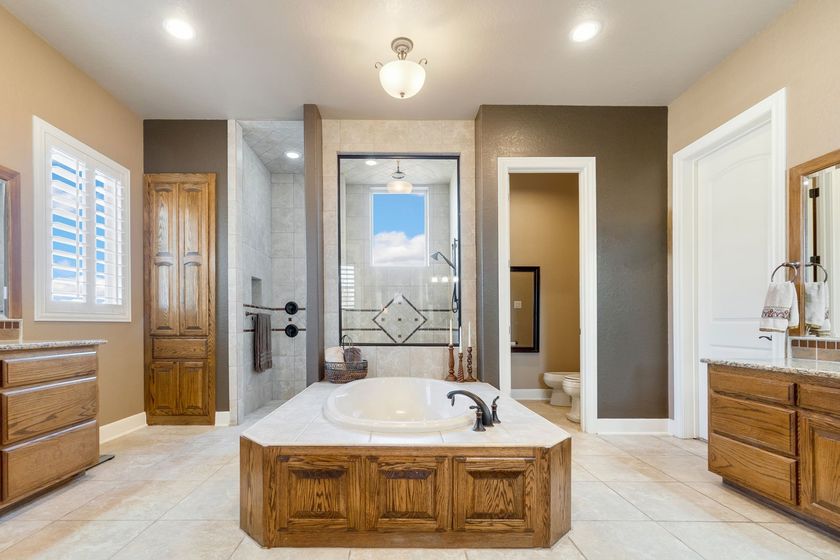 Modern bathroom with a central soaking tub, glass shower, and wood vanities in a neutral-toned space