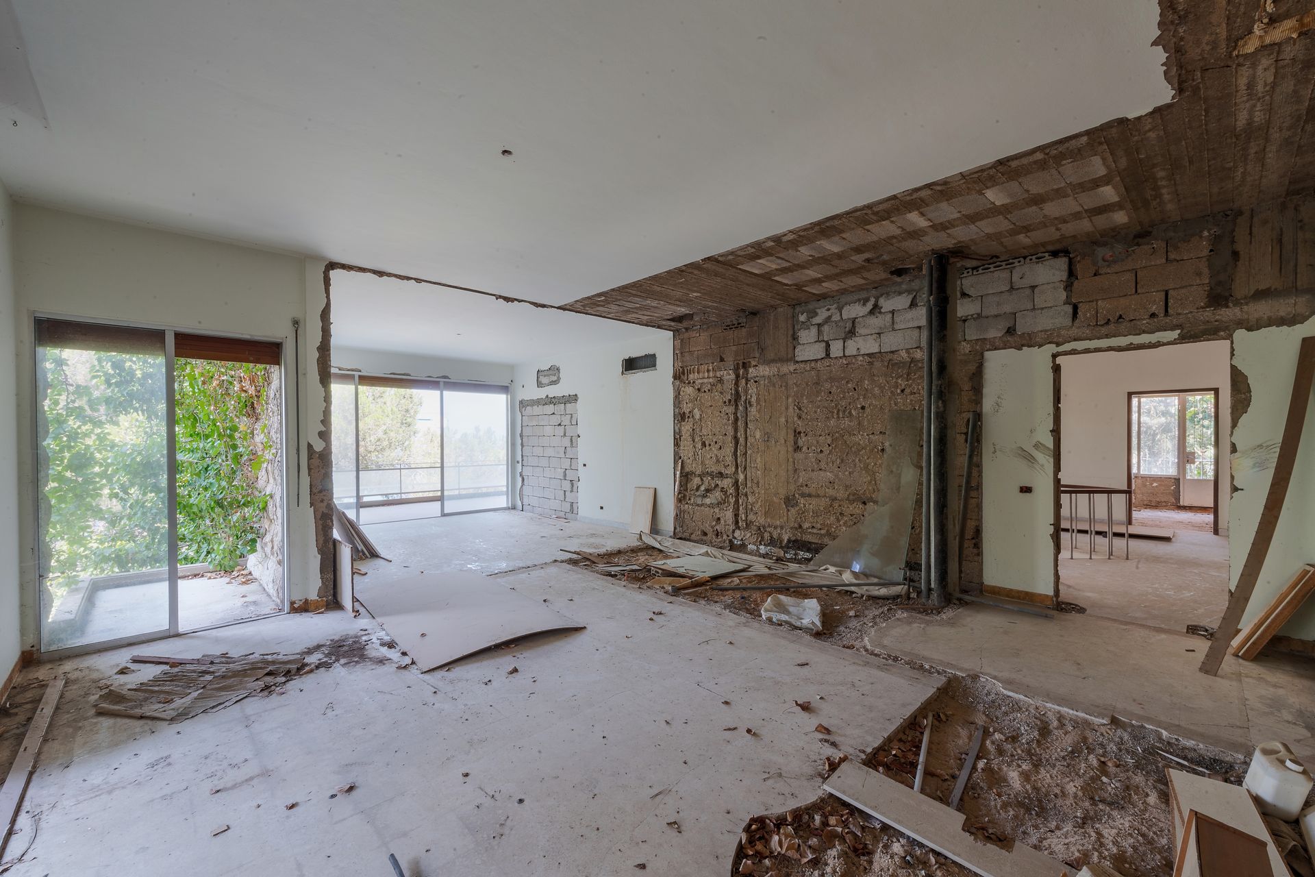 Damaged interior room with exposed brick, debris on the floor, and large windows