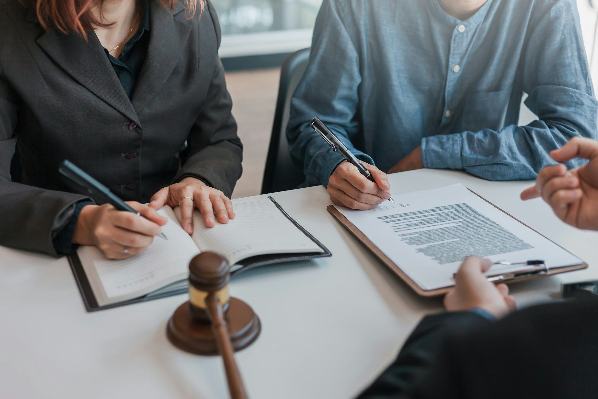 Three people review documents at a desk with a gavel, suggesting a legal consultation or meeting.