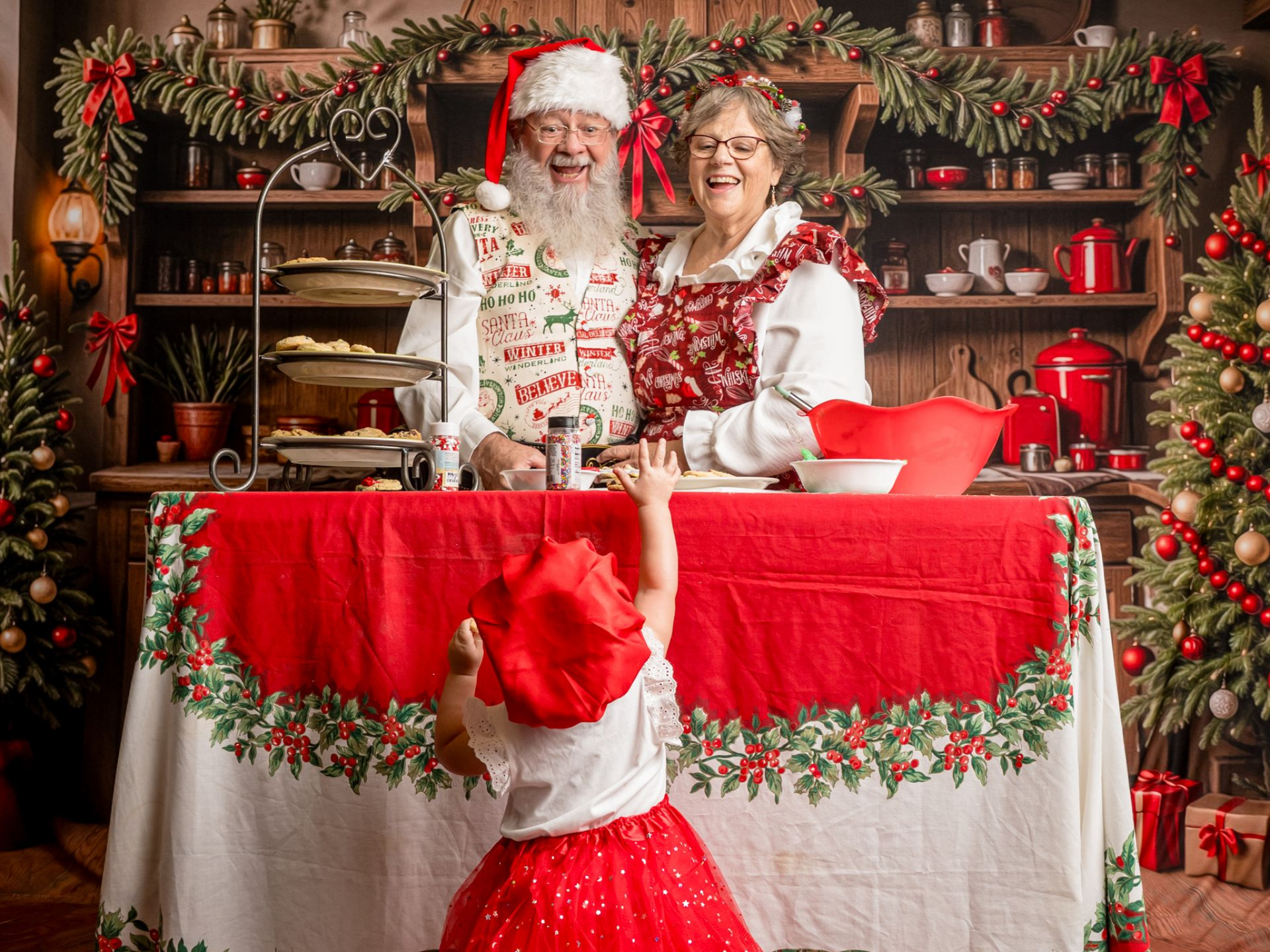 Santa and Mrs. Claus in the kitchen with child reaching for cookies.