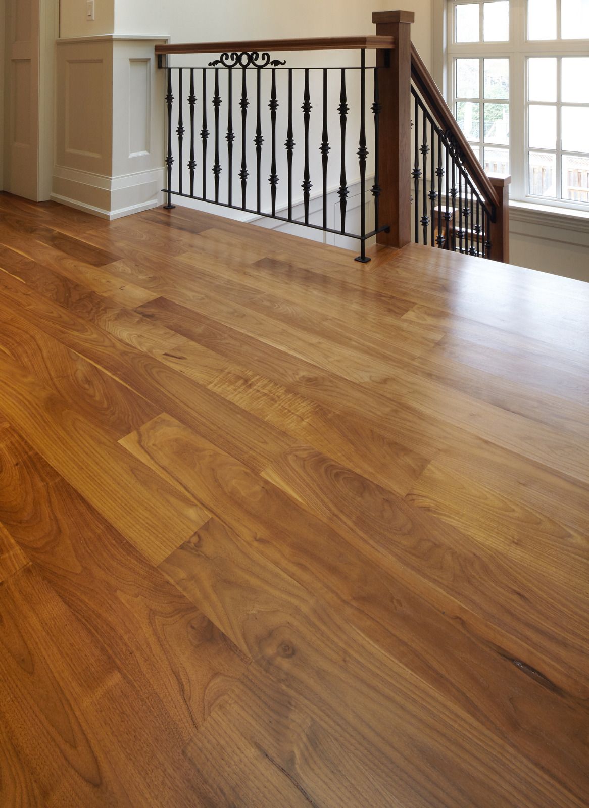 A wooden floor next to a staircase with a wrought iron railing.