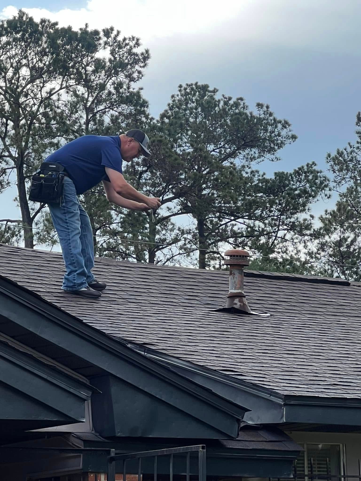 Worker on a shingled roof inspecting or repairing shingles near a vent pipe