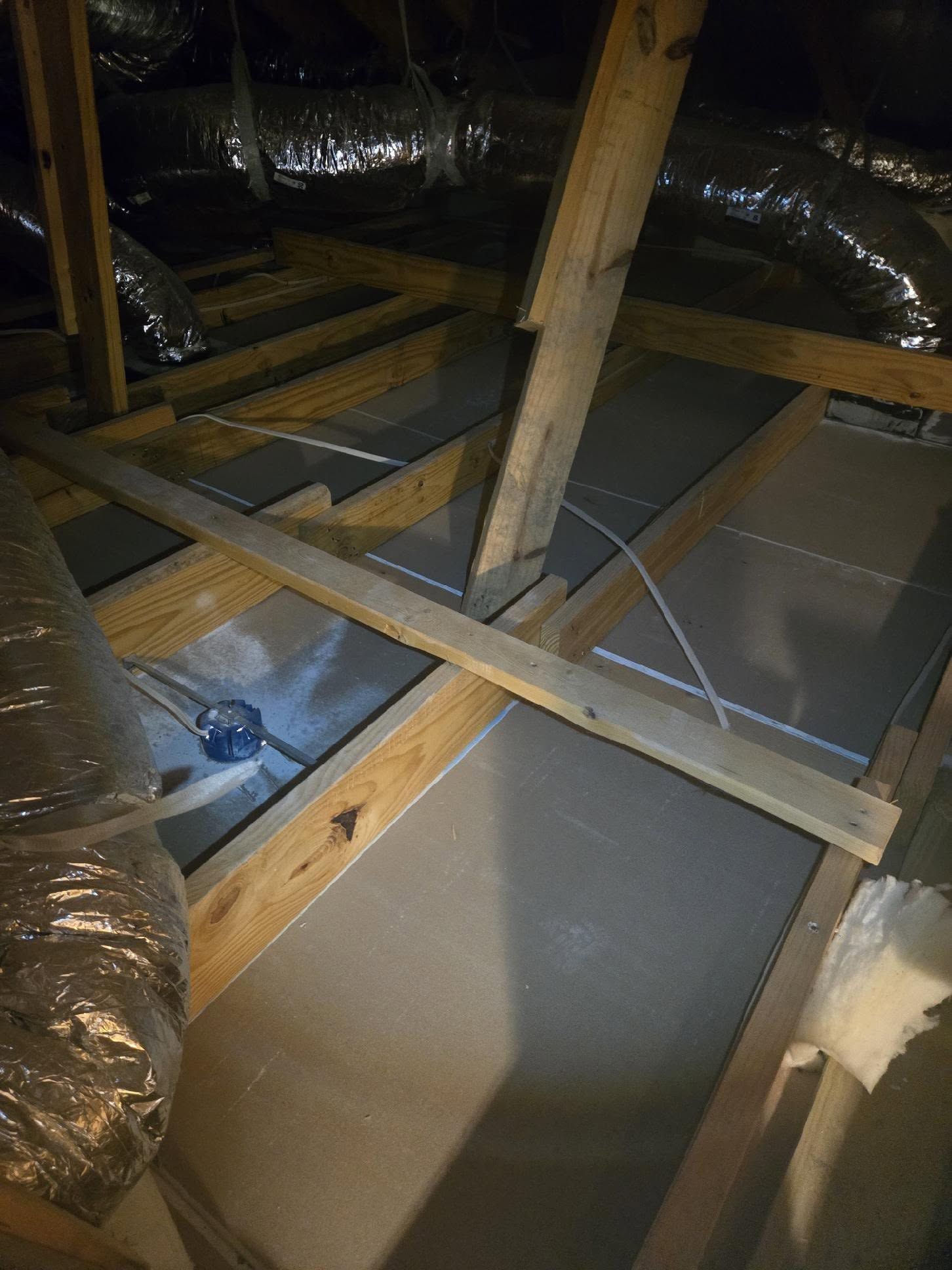 Attic with exposed wooden rafters, insulation ducts, and a gray board floor panel
