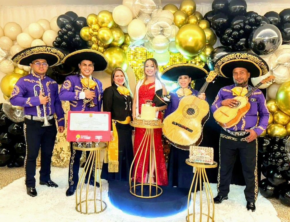 Banda de mariachis con mujer junto a un pastel, globos en dorado, negro y blanco.