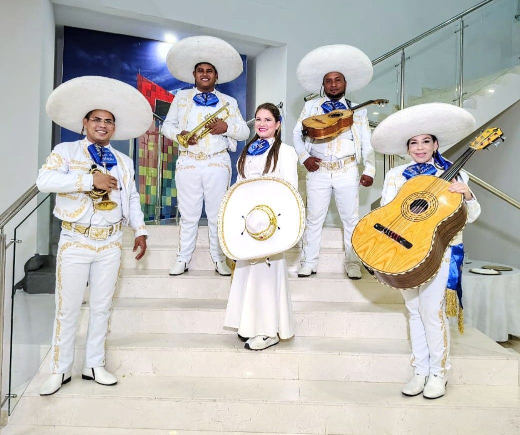 Banda de mariachis con trajes blancos en las escaleras, sosteniendo instrumentos y un escudo redondo.