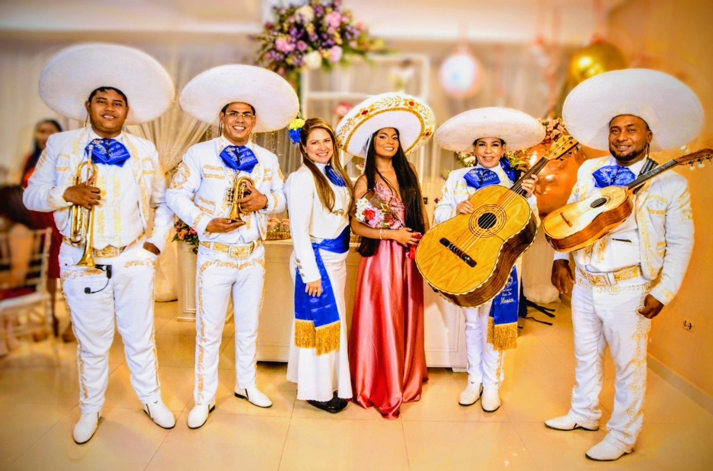 Mariachi con dos mujeres al frente. Los músicos visten trajes blancos y sombrero