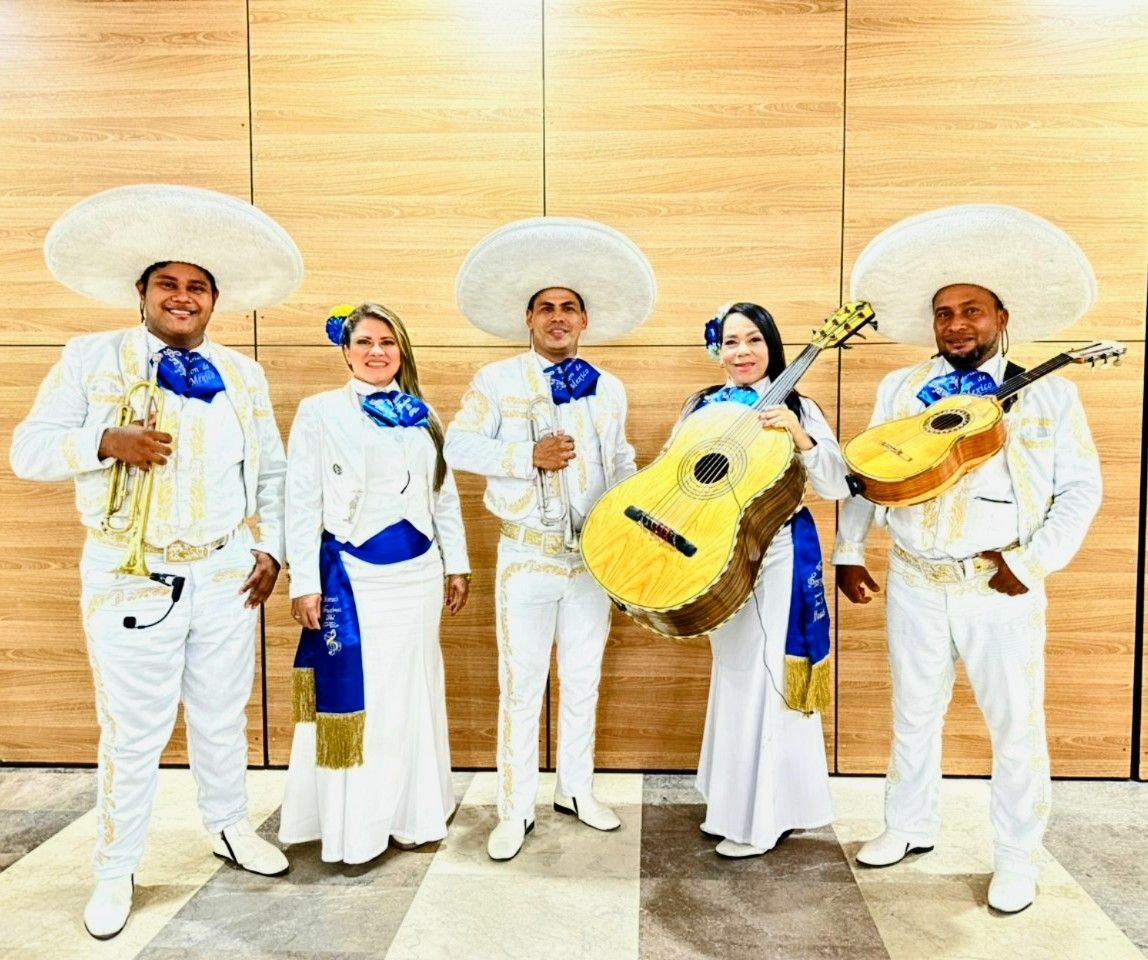 Cinco personas vestidas con trajes blancos de mariachi, sosteniendo guitarras, posando frente a un fondo neutro.