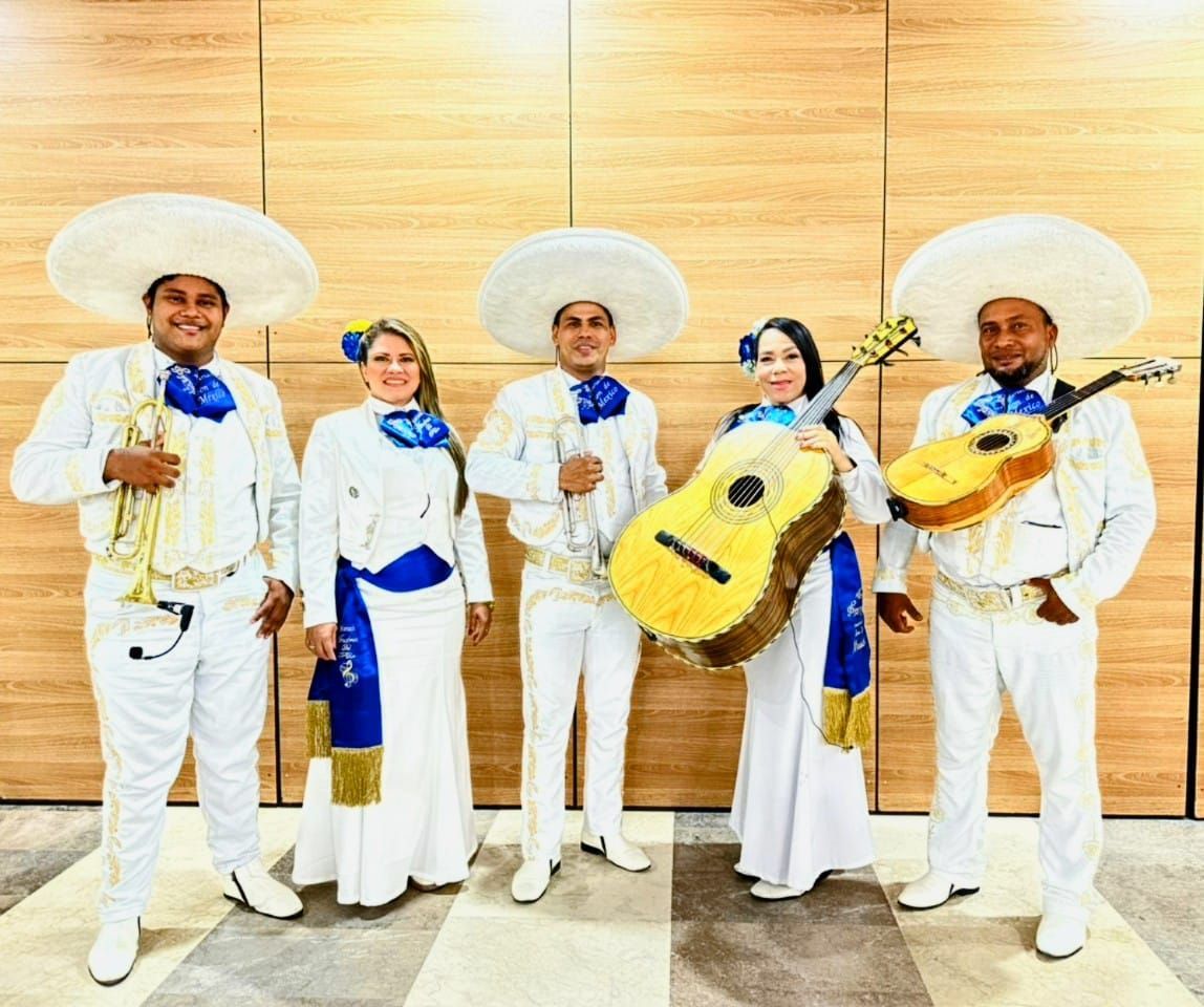 Banda de mariachis con trajes blancos y azules, sosteniendo guitarras y sonriendo.