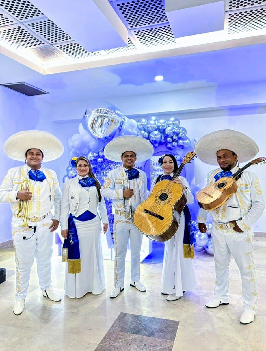Banda de mariachis con trajes blancos y azules, tocando instrumentos en una habitación decorada.