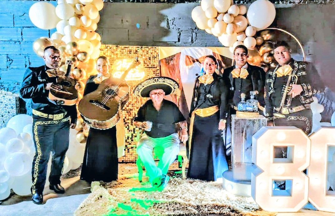 Banda de mariachis tocando en una fiesta, con globos y cartel iluminado 