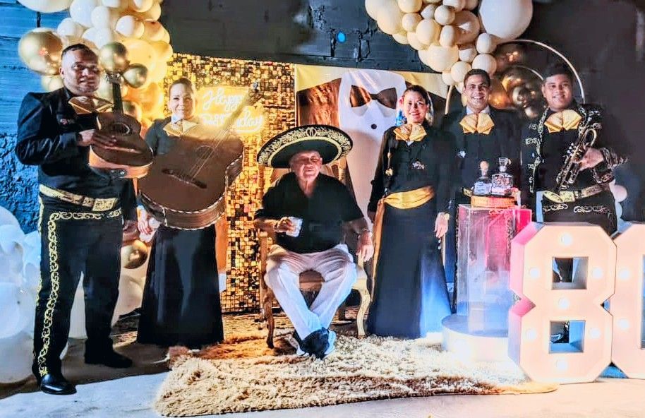 Banda de mariachis con cumpleañero frente a decoraciones doradas y números 