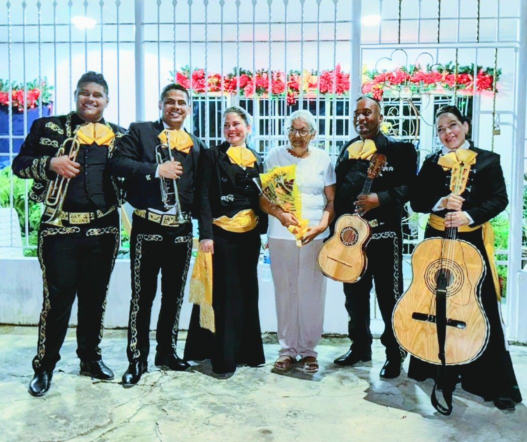 Mariachi con una mujer sosteniendo flores. Los músicos visten trajes negros