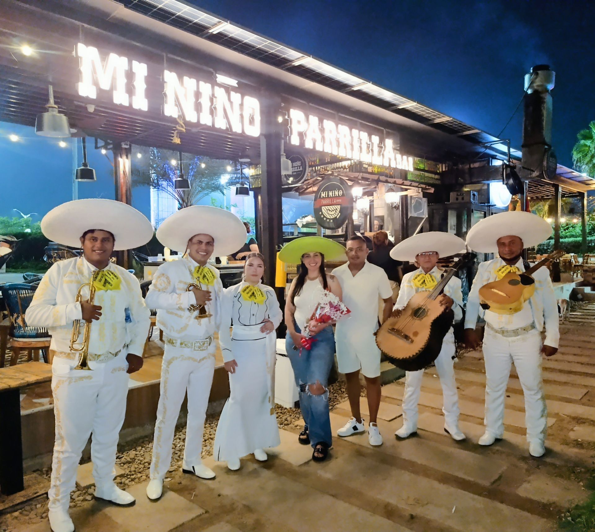 Banda de mariachis y dos personas posan afuera del restaurante 