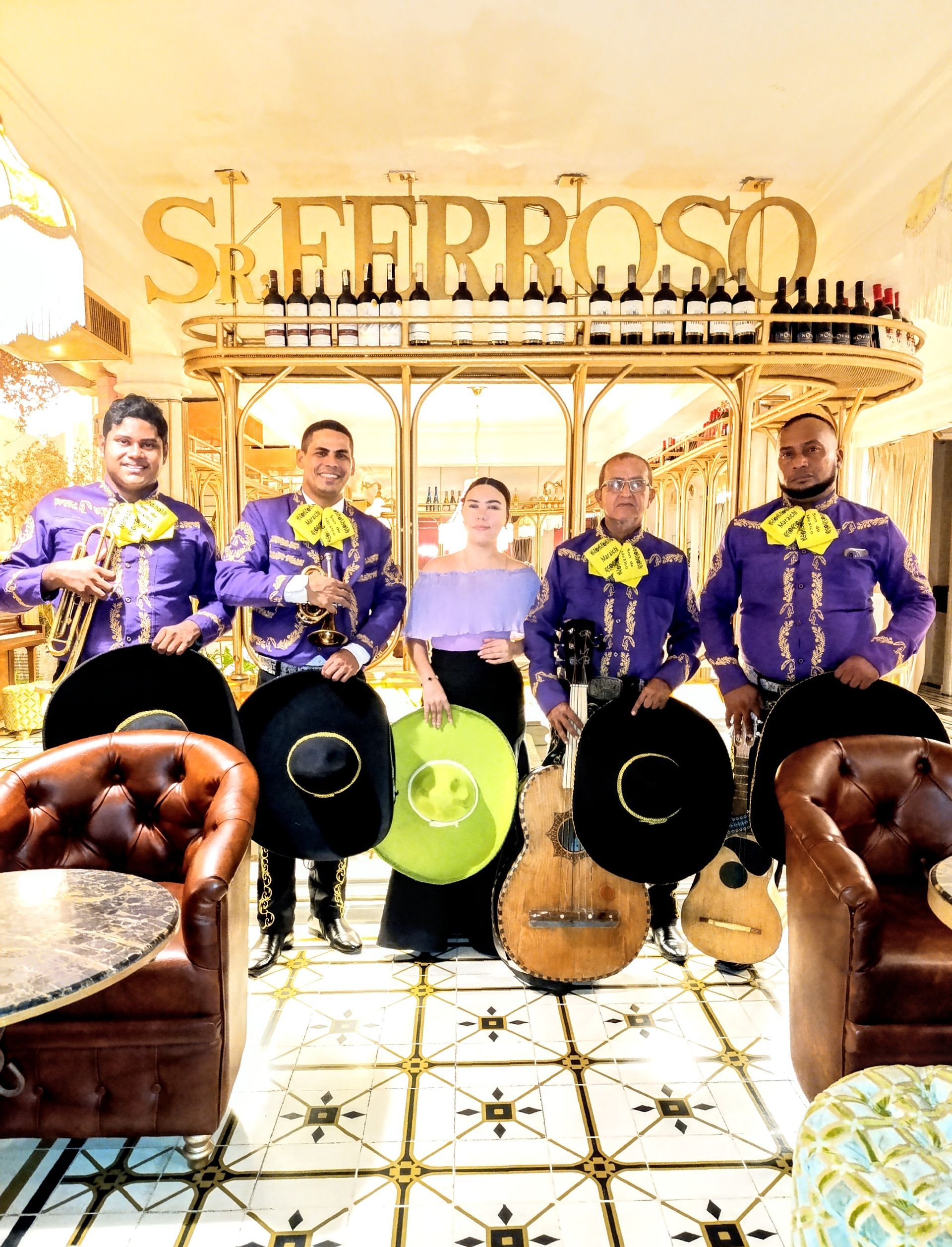 Banda de mariachis con trajes morados, sosteniendo instrumentos, posando frente a un bar.