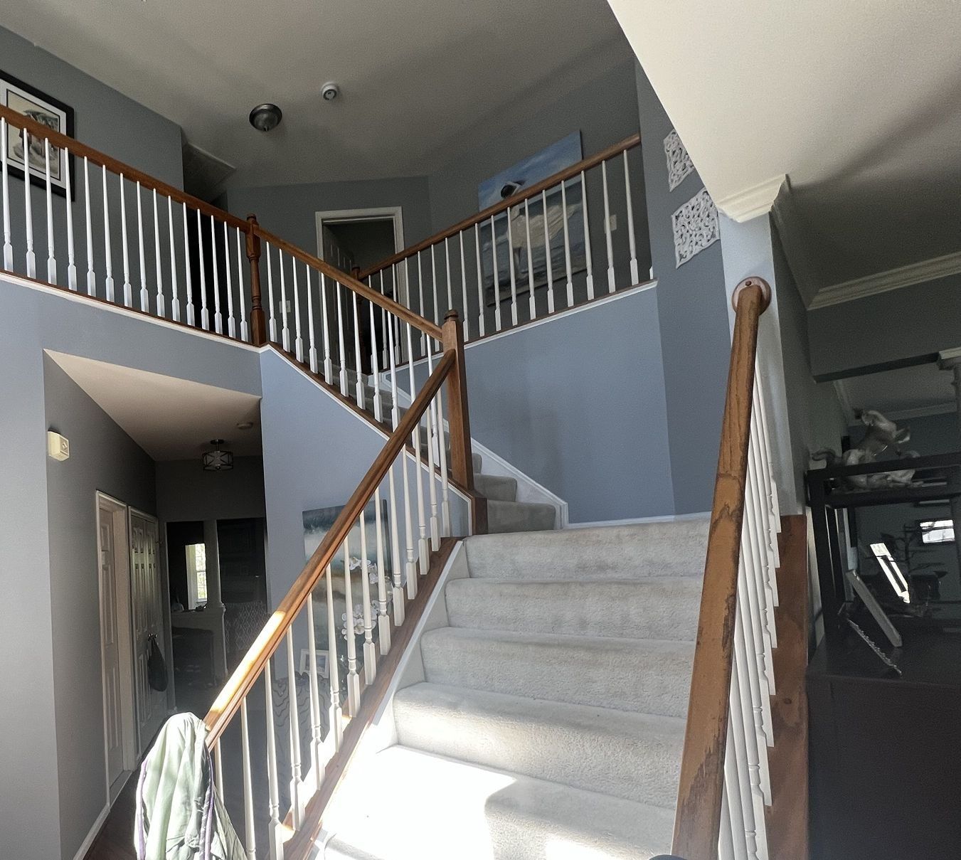 Before: carpeted two-story foyer stair with oak rail and spindles