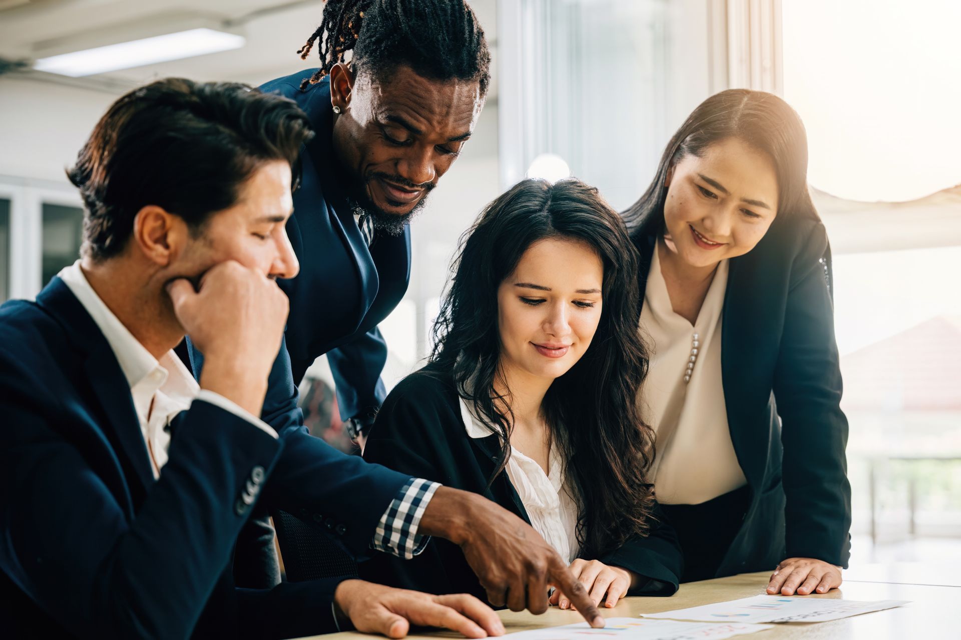 Four diverse professionals review paperwork together in a modern office.