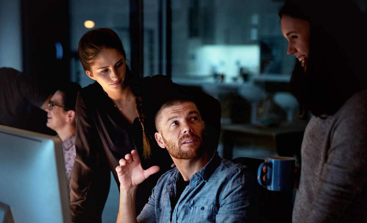 Team members collaborating at computers in a dimly lit office.