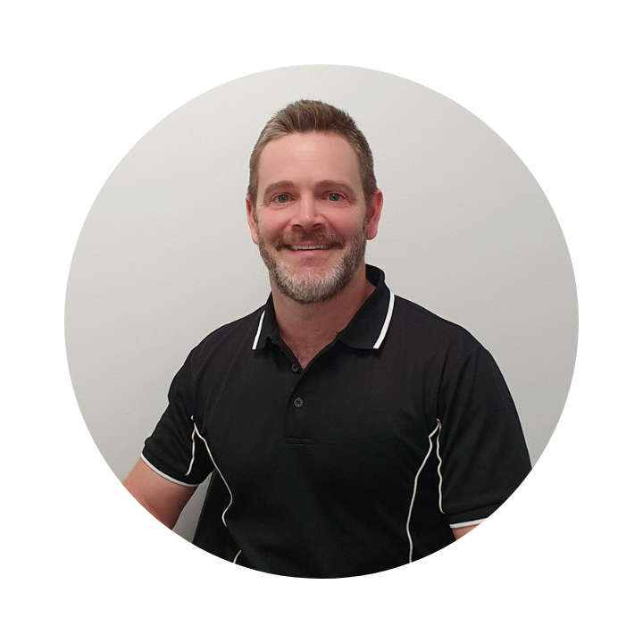 Man with a beard in a black polo shirt smiles in front of a white wall.