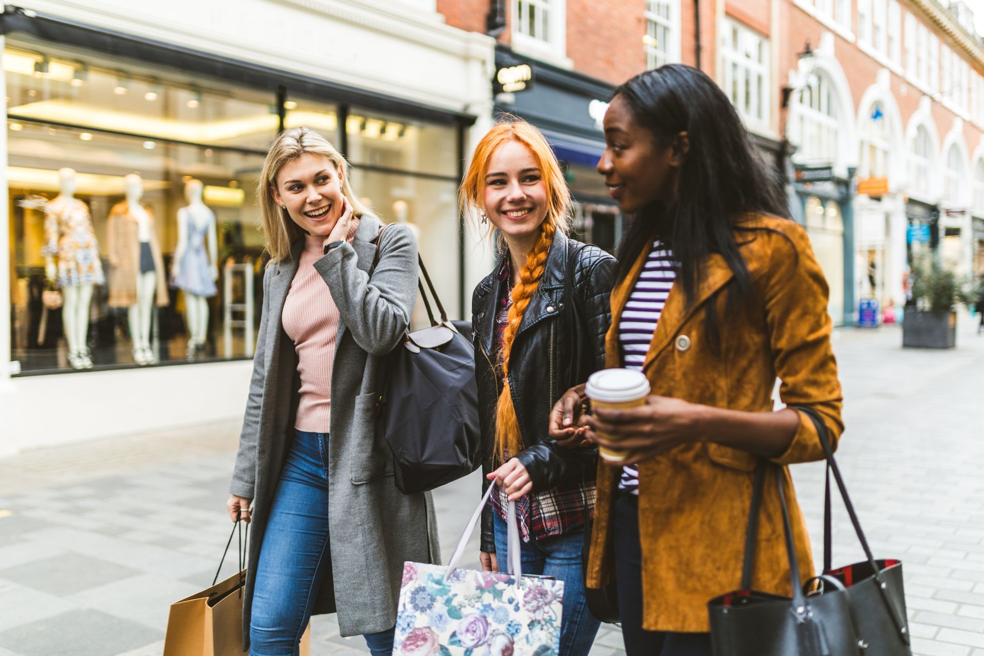 Three women walking and smiling with shopping bags outside storefronts