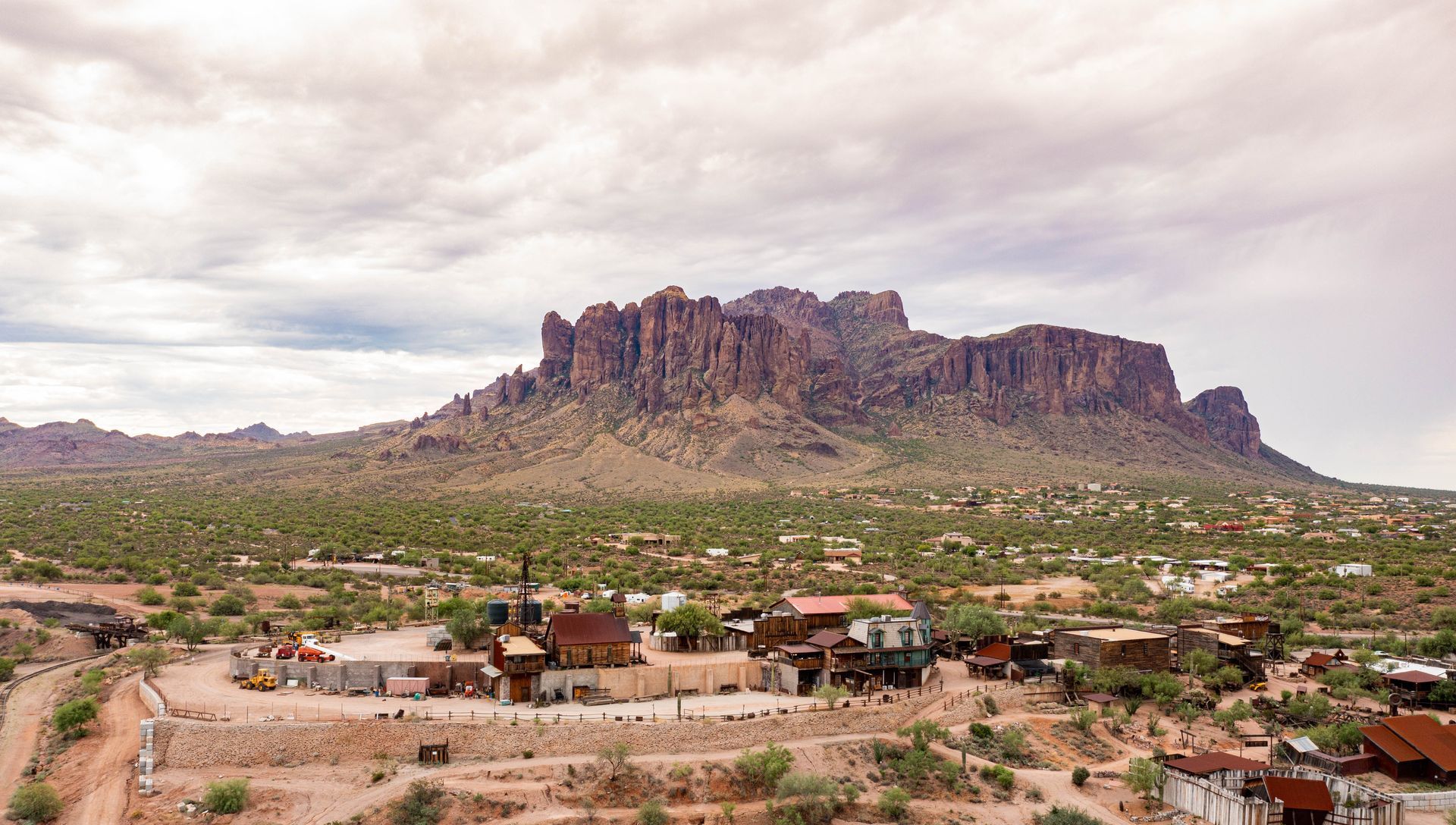 Desert town beneath a rocky mountain range under cloudy skies