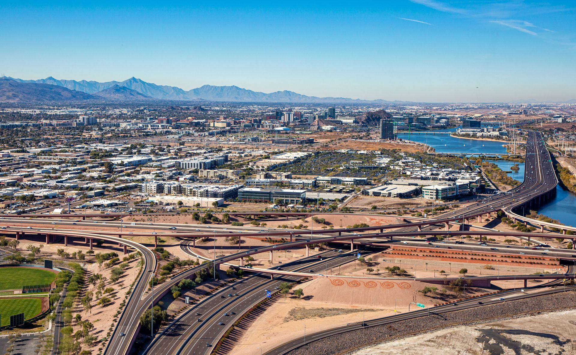 Wide aerial view of a sprawling desert city with highways, buildings, and mountains in the distance