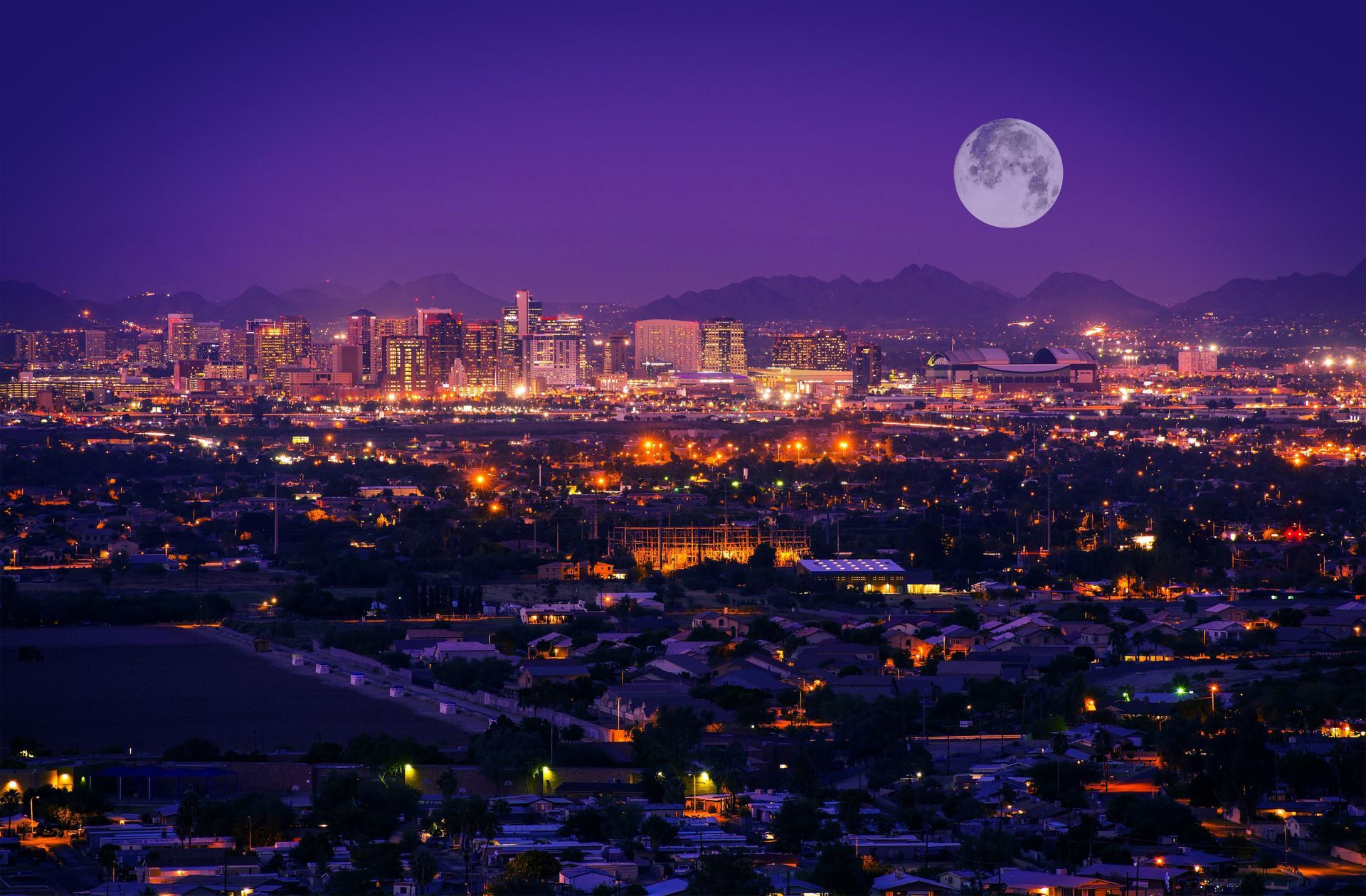 Moonlit city skyline at dusk with glowing lights and purple sky