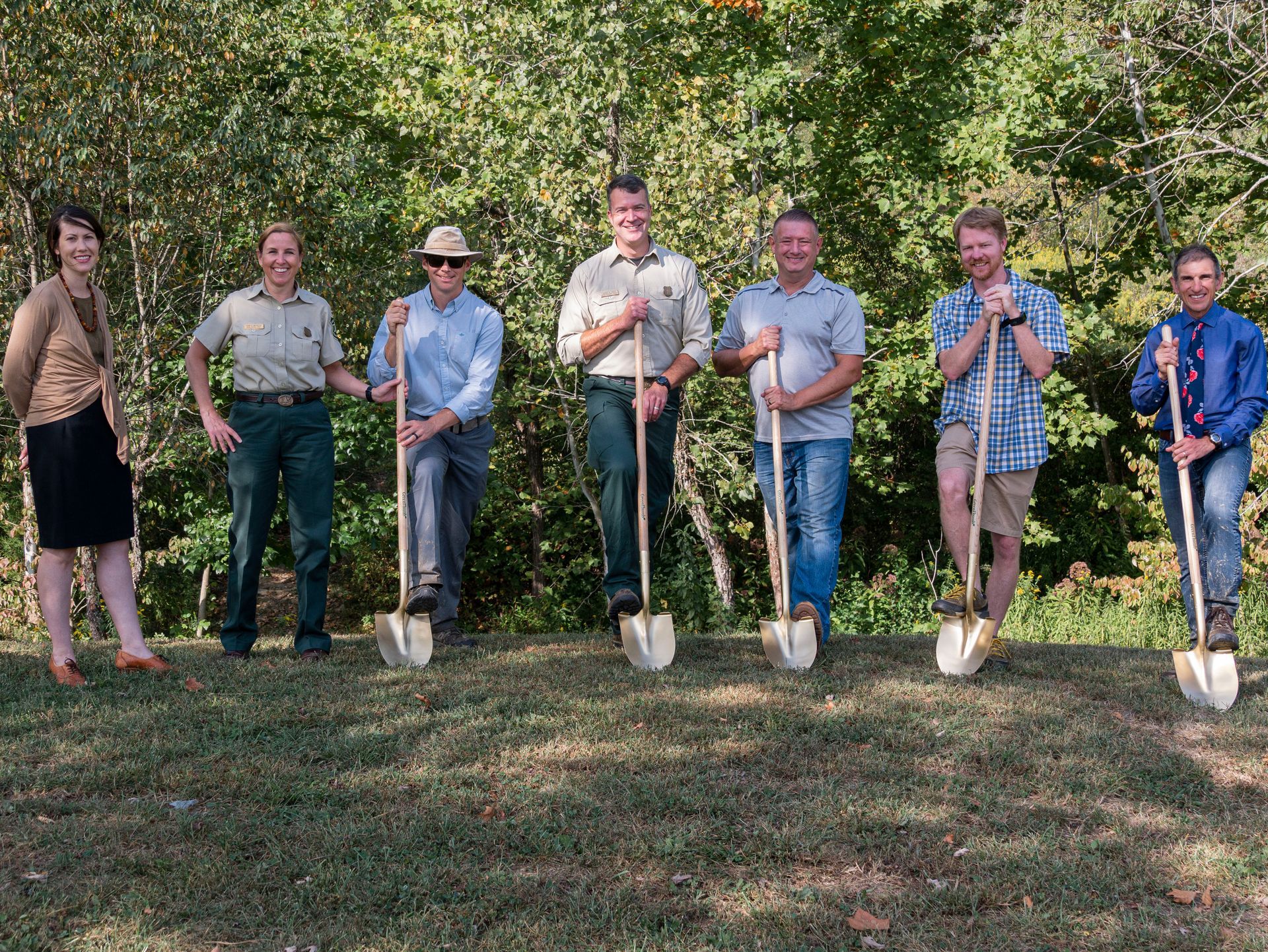 A group of people are standing in a field holding shovels.
