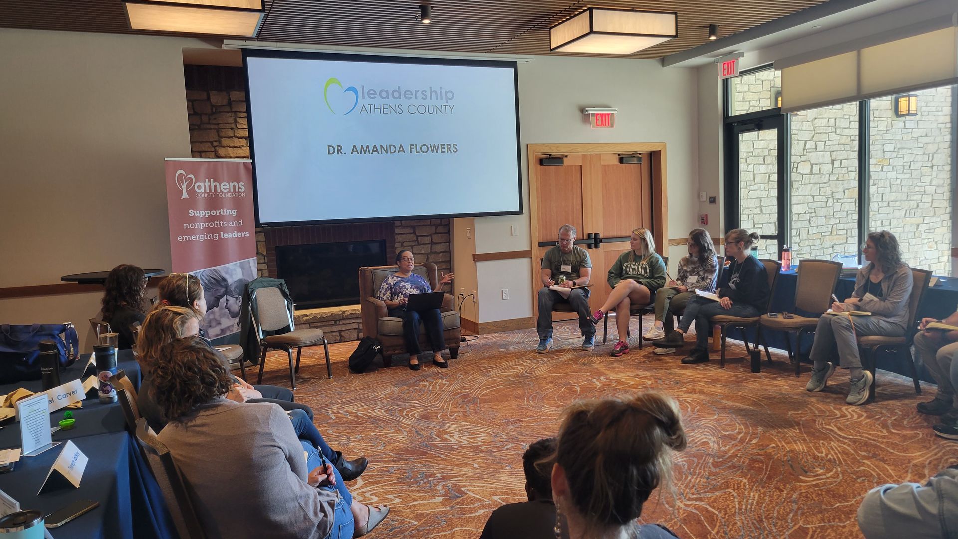 A group of people are sitting in a circle in front of a projector screen.