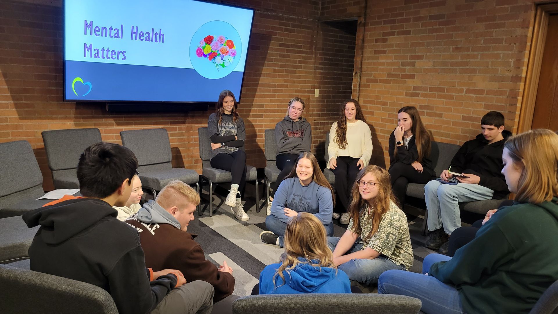 A group of people are sitting in a circle in front of a television.