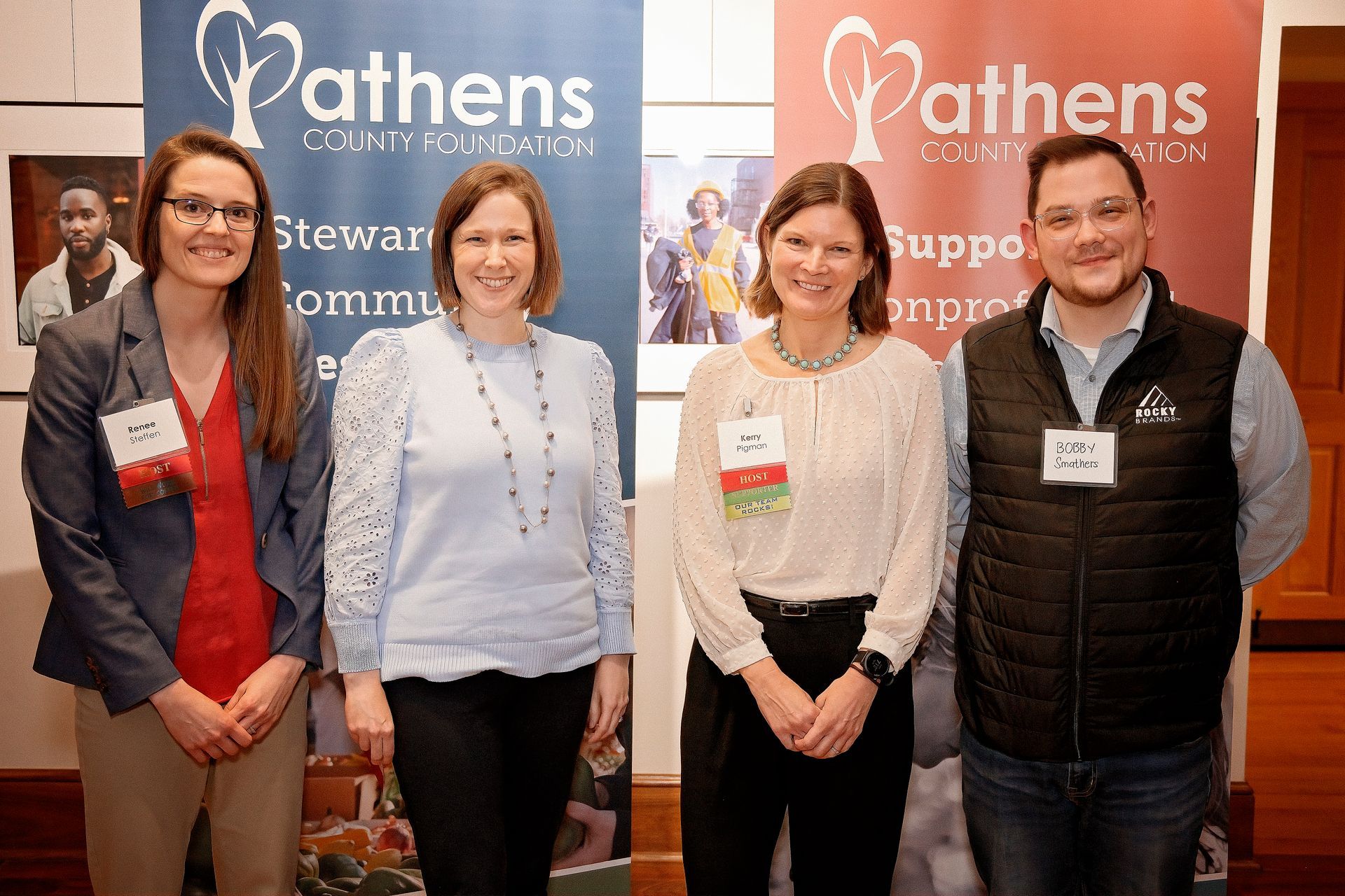 Four people pose in front of Athens County Foundation banners. Two women and two men smiling, indoors.