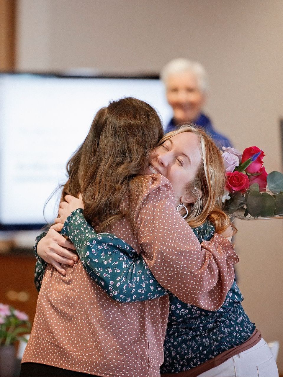 Two women are hugging each other in a room.