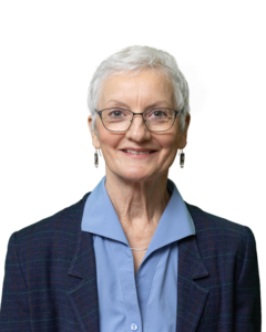 Woman with short white hair, glasses, smiling, wearing blue shirt and blazer.