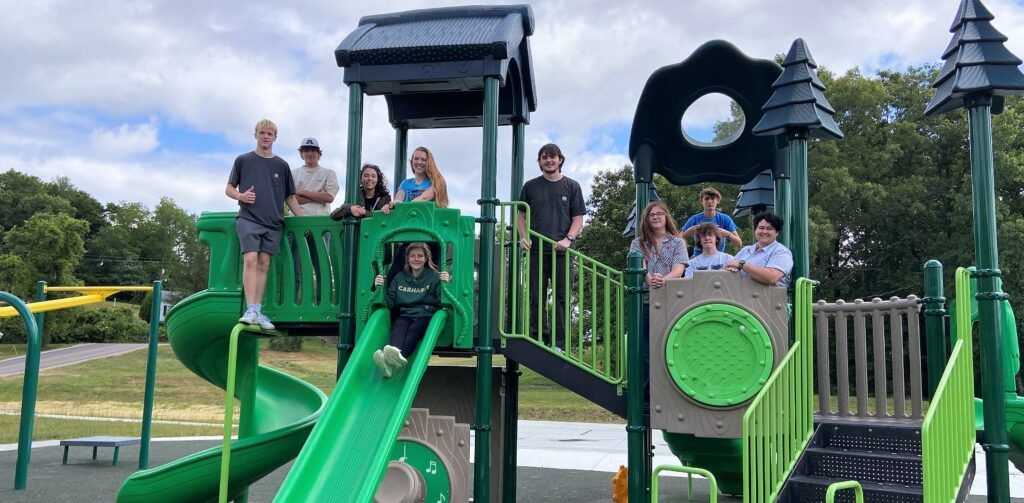 Group photo of 10 people on green playground equipment, standing and smiling.