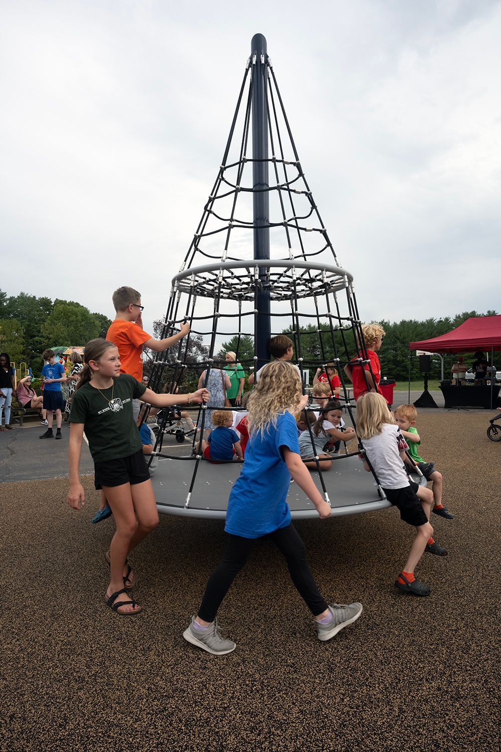 Children playing on a black and gray climbing structure at a park, some are pushing it while others climb.