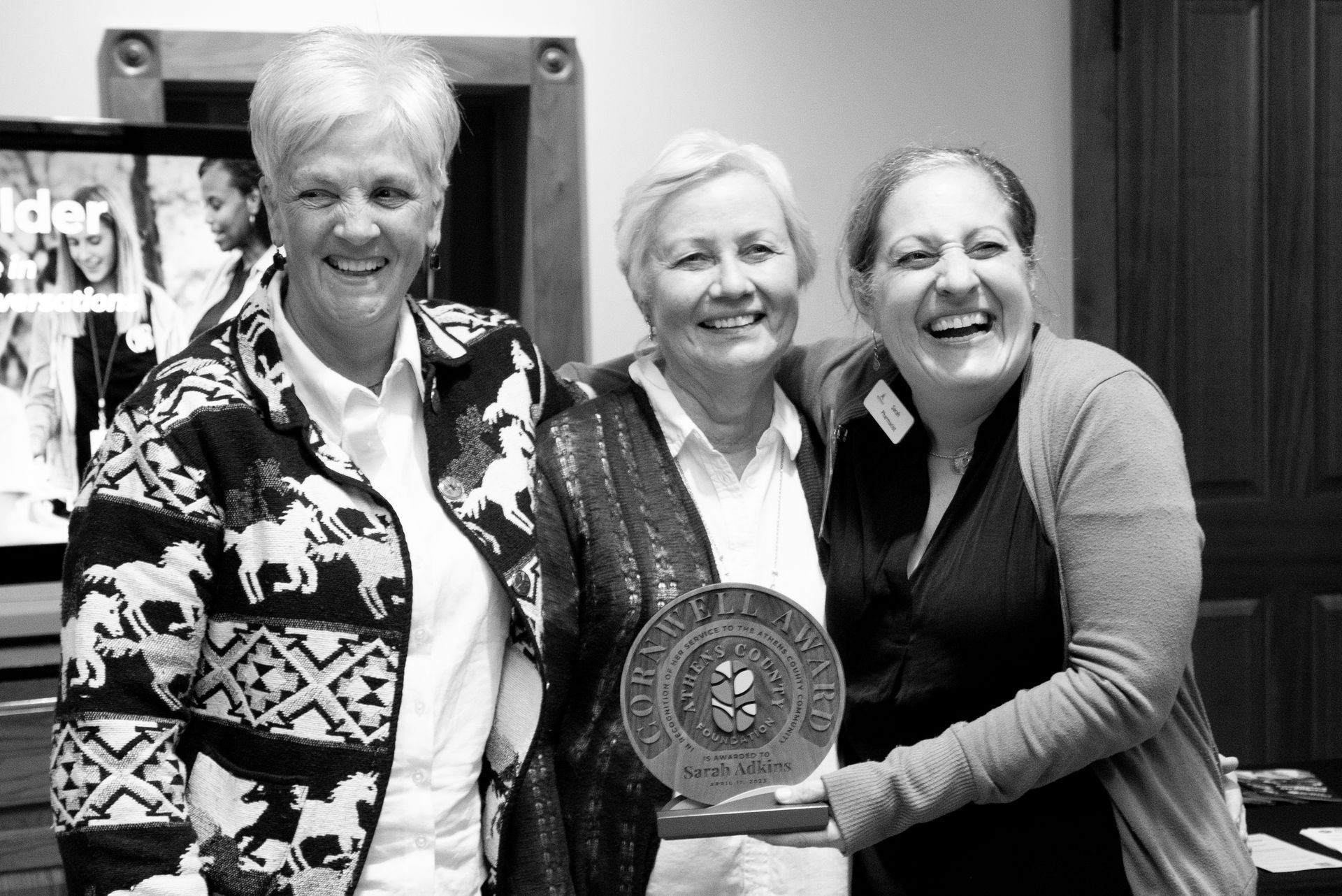 Three smiling women holding an award, indoors. Athens County, OH