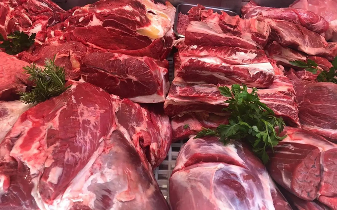 Tagli di carne rossa cruda disposti su un vassoio con guarnizione di prezzemolo al banco di una macelleria.