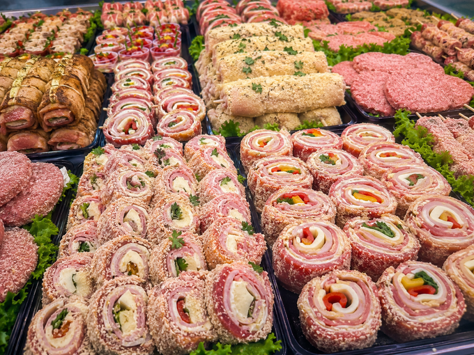Vari tipi di involtini e polpette di carne cruda ripieni, esposti in file ordinate su un banco del mercato.