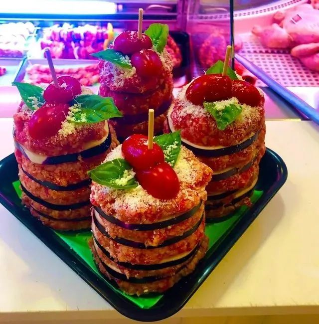 Pasticcini impilati, guarniti con ciliegie e menta, disposti su un vassoio nero in una vetrina colorata.