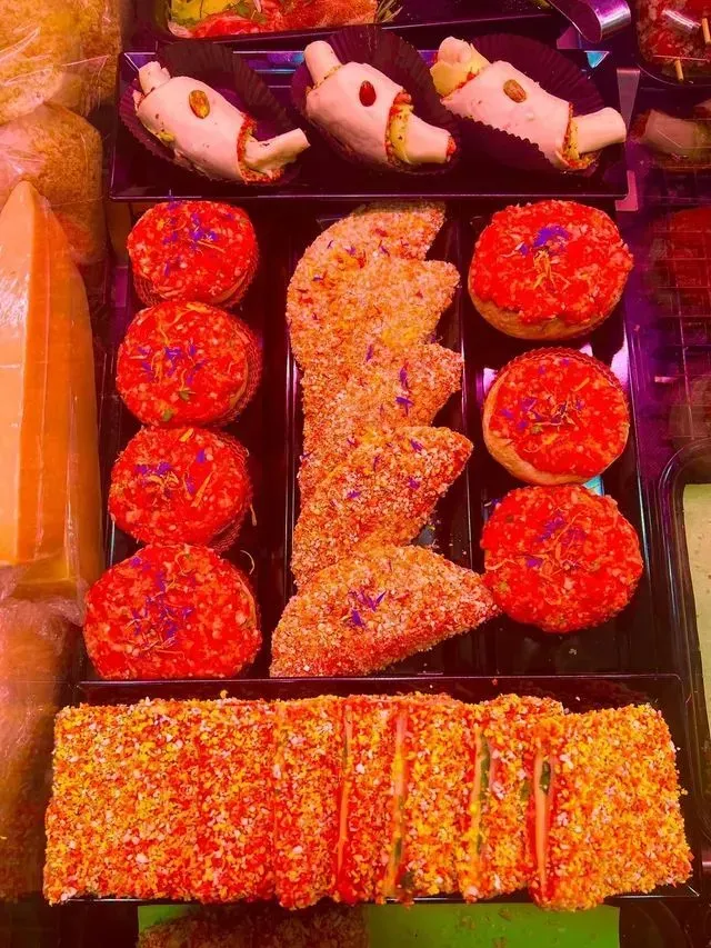 Un assortimento di dolci e pasticcini colorati disposti su un vassoio, tra cui dolcetti rosa e dolcetti rotondi rossi.