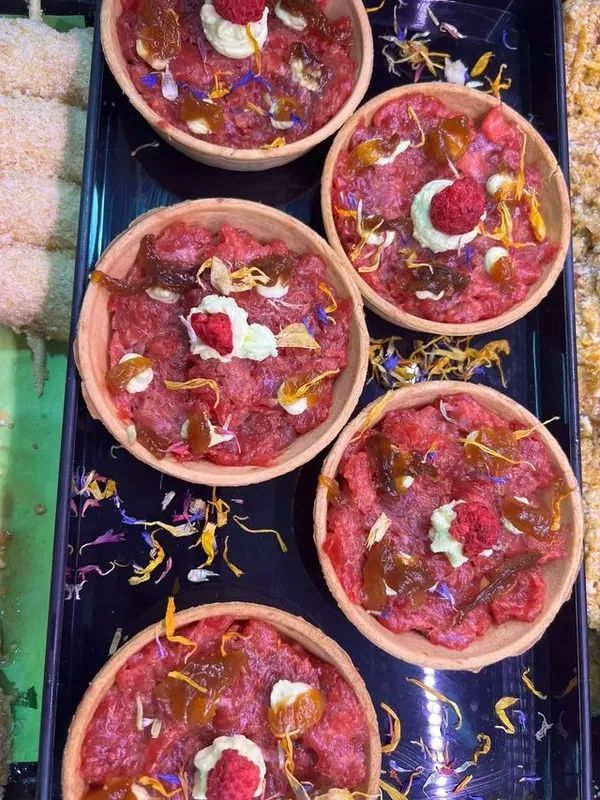 Cinque piccole crostatine rotonde guarnite con frutti rossi e panna, disposte su un vassoio decorativo.