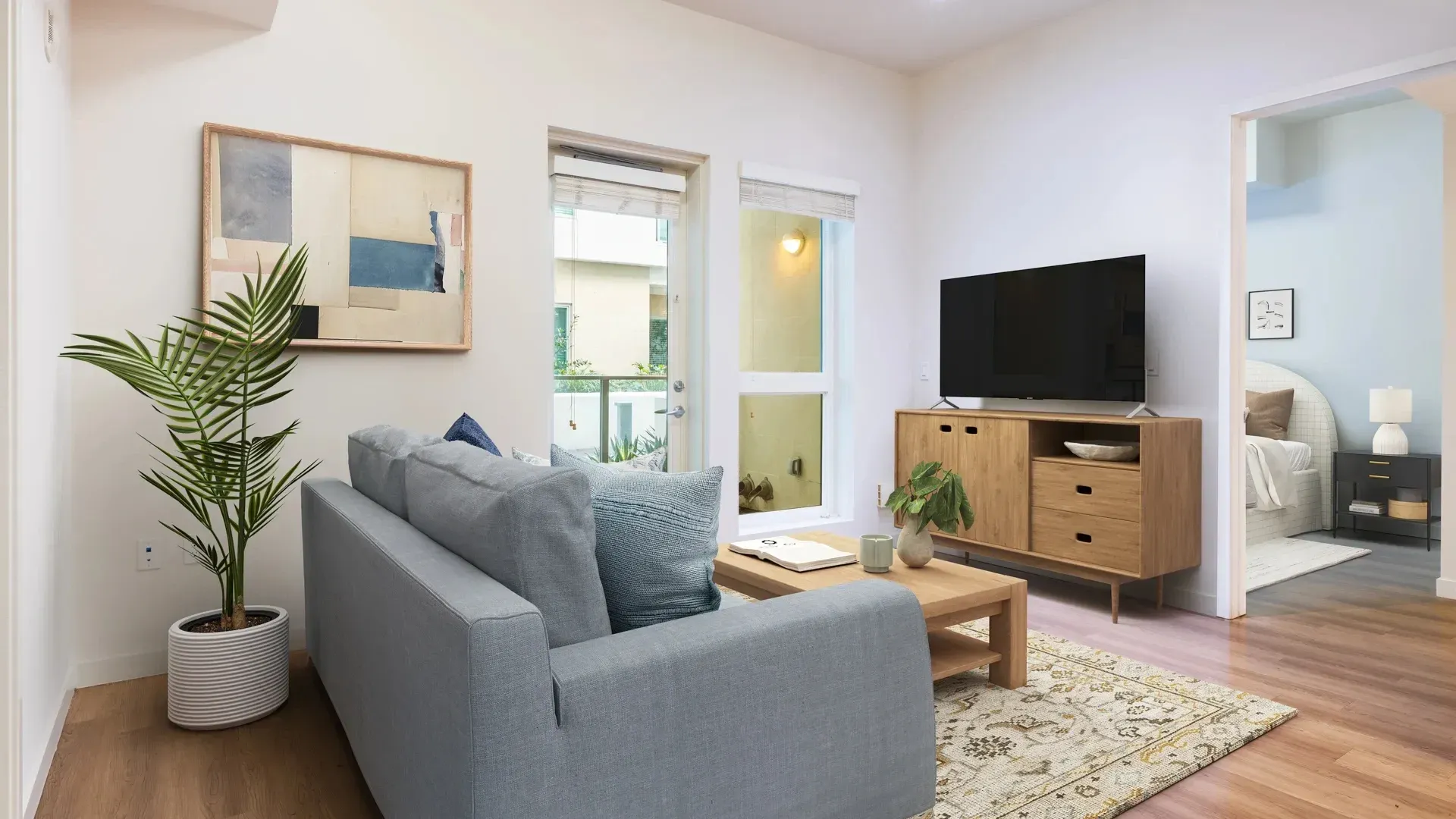 Modern living room with sofa, coffee table, TV, and artwork, leading to a bedroom.