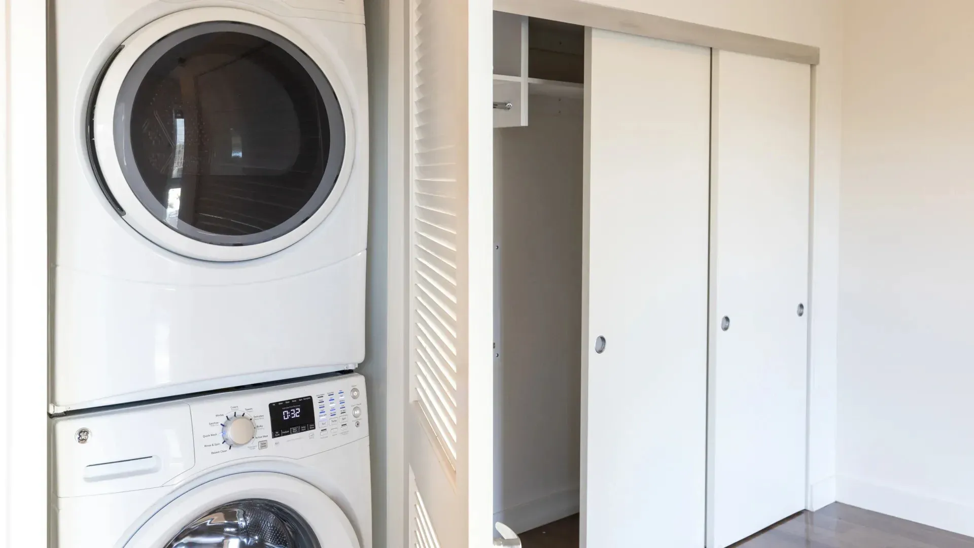 Stacked washer and dryer unit next to a closet with sliding doors.