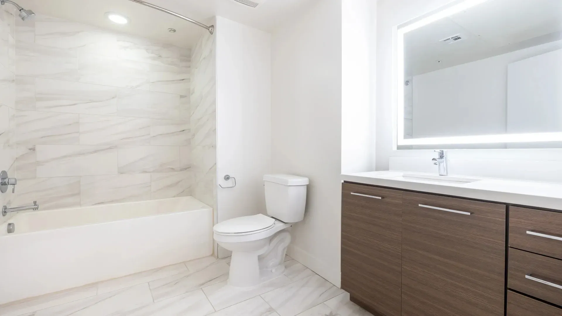 Modern bathroom with vanity, illuminated mirror, bathtub, and toilet.