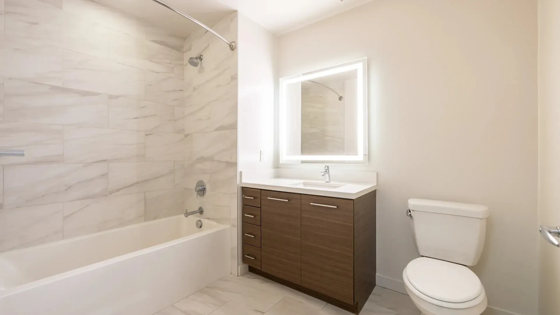 Modern bathroom with a white bathtub, vanity with a backlit mirror, and a toilet.