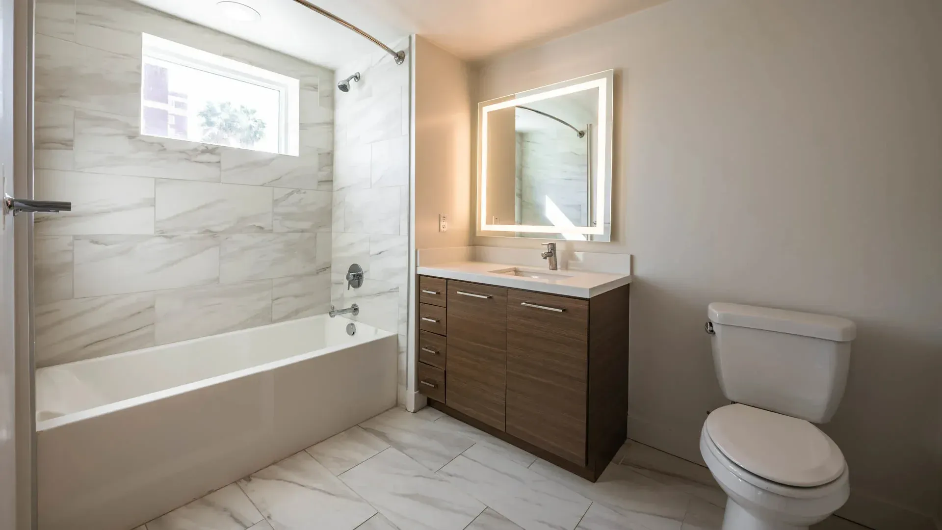 Modern bathroom with a large vanity and illuminated mirror, bathtub, and toilet.