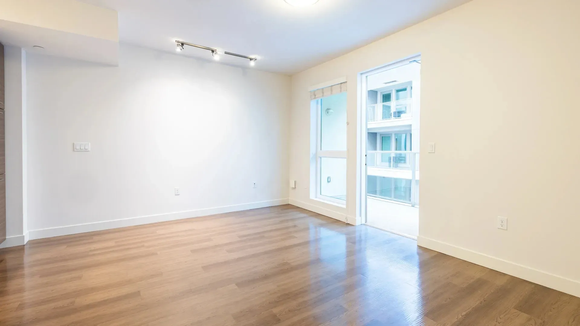 Empty living room with wood floors and a sliding glass door leading to a balcony.