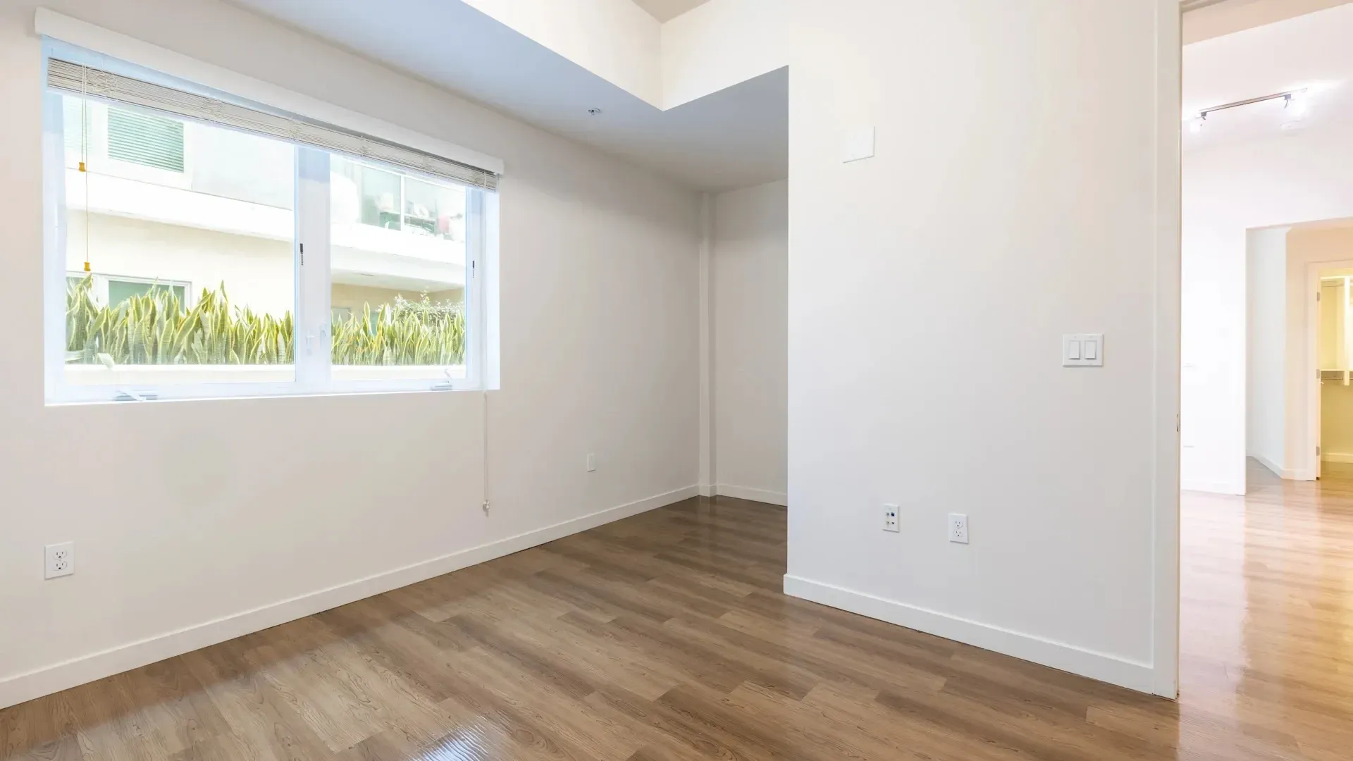 Empty bedroom with large window and wood floors.