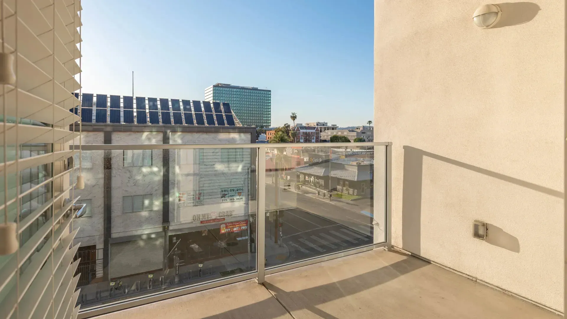 Balcony with a view of the city skyline, blinds on the left, and a wall with a light fixture on the right.