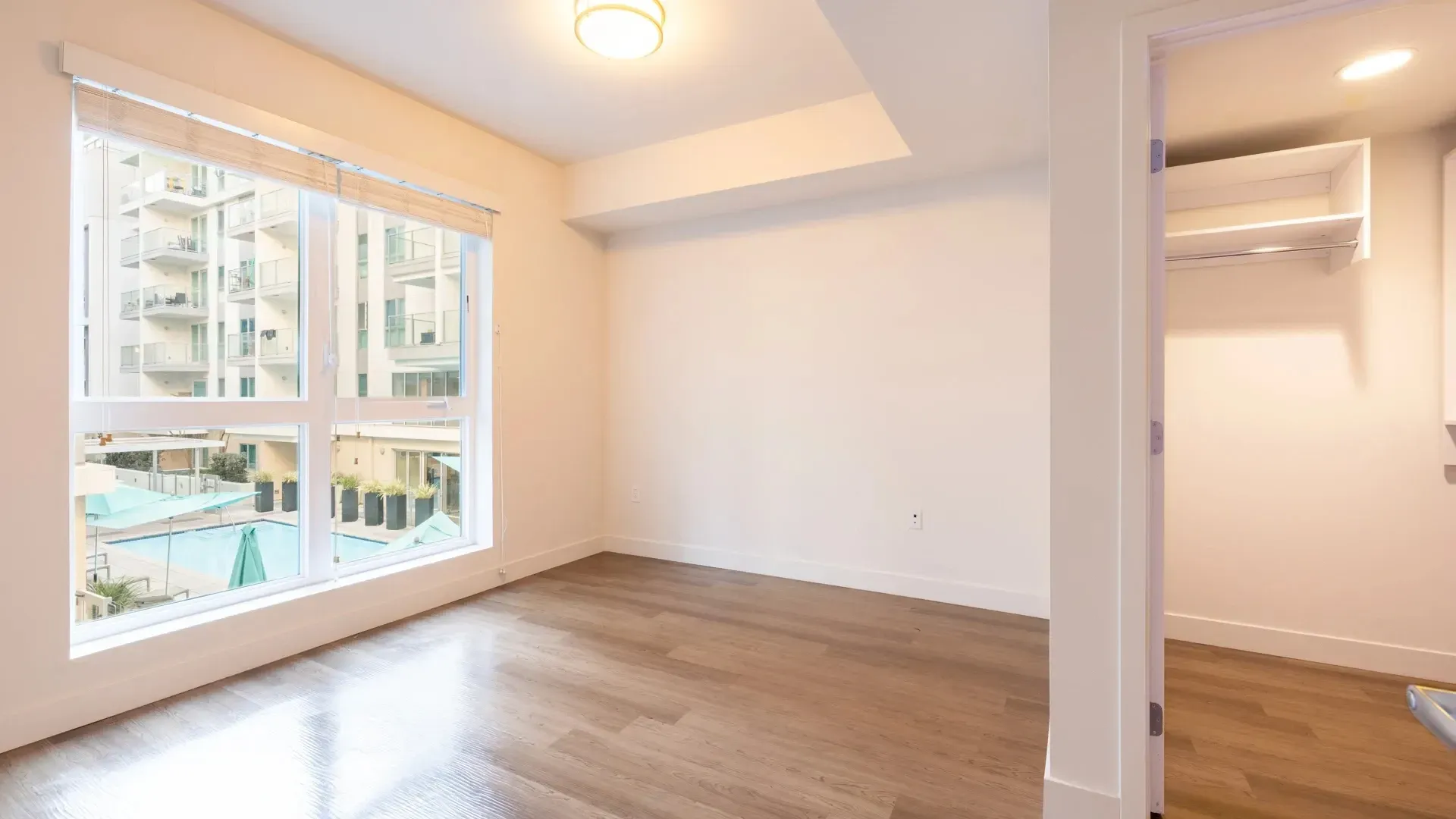 Interior view of an empty apartment with a large window overlooking a pool and building exterior.