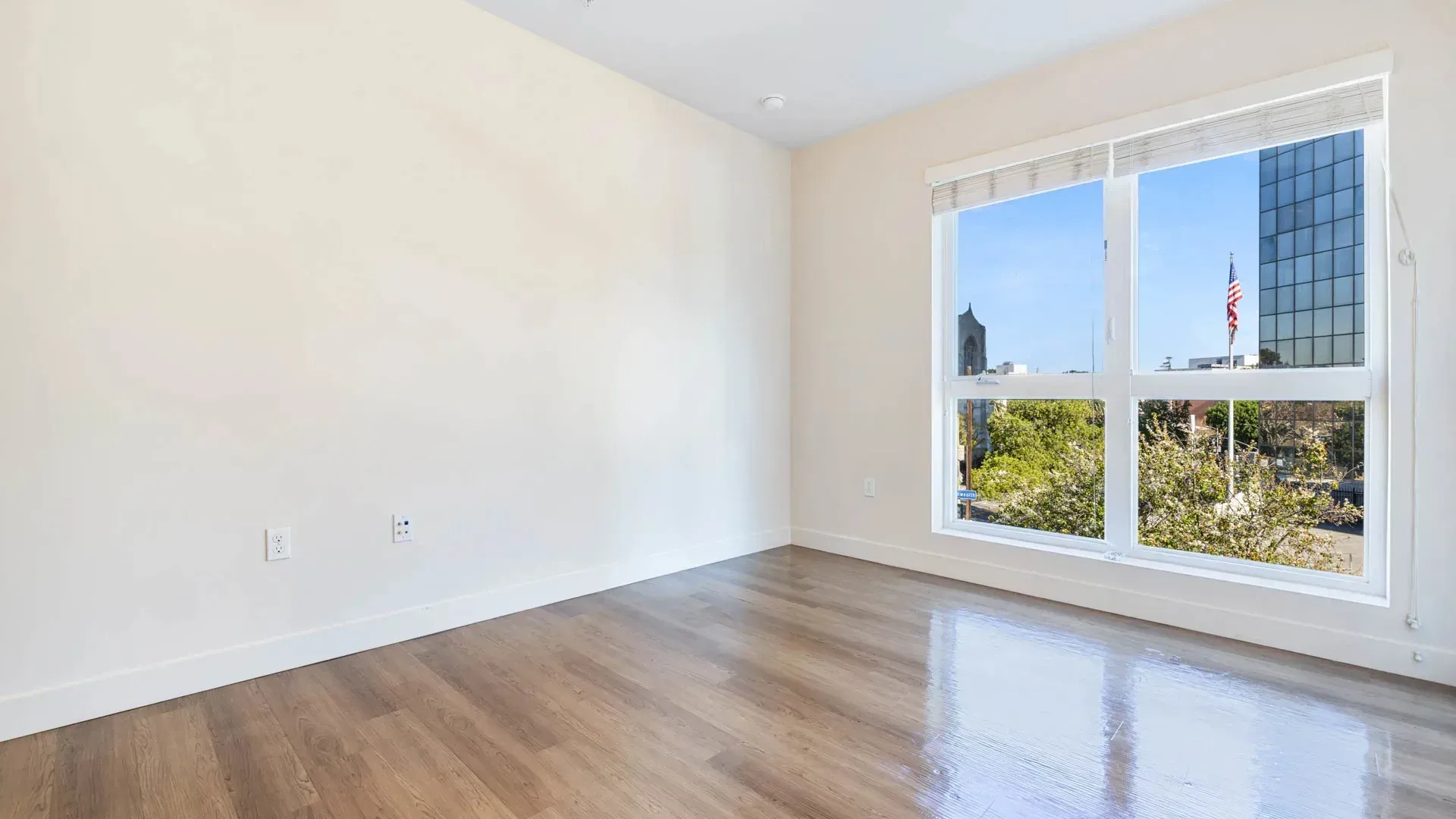Empty room with hardwood floors and a large window overlooking a city view.